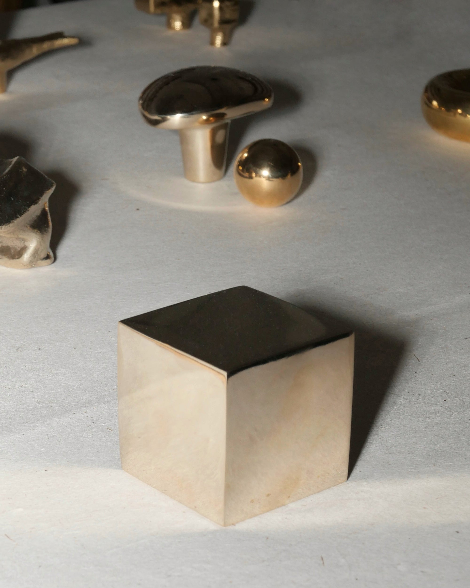 Gold metallic cube on a textured white surface with other metallic objects.